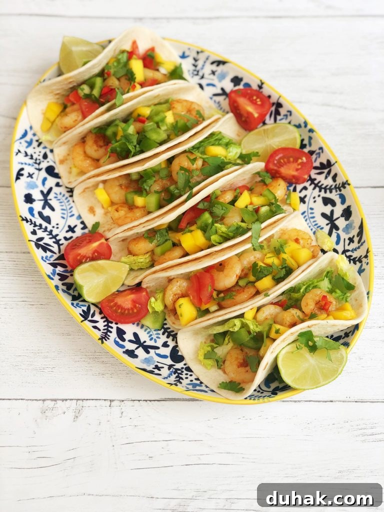Homemade Cajun prawn tacos with spicy mango salsa garnished with lime wedges and tomatoes.