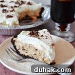 slice of cold brew coffee pudding pie on a white textured plate with a fork and a cup of coffee in the background