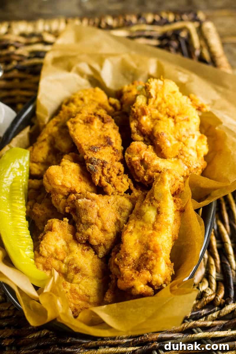Pickle Brined Keto Fried Chicken in a basket with brown parchment paper and a pickle spear and some garlic mustard aioli.