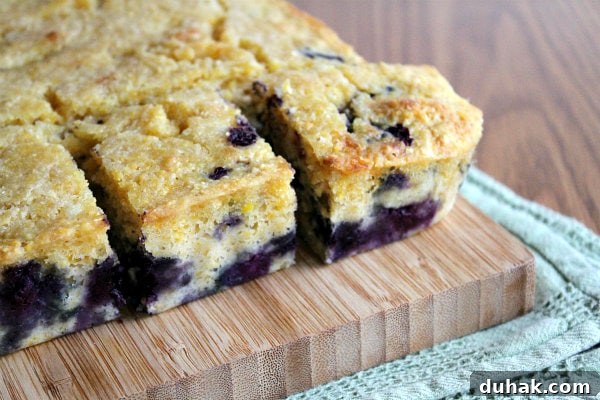 blueberry cornbread cut into pieces on a cutting board set on a green cloth napkin