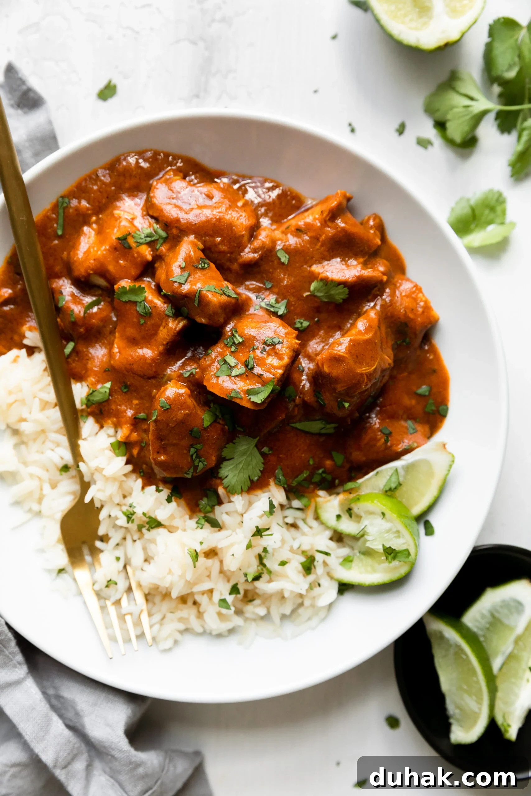 Chicken Tikka Masala Recipe: Light, Flavorful Weeknight Meal 2 cubes of chicken smothered in tikka masala sauce over a bed of white rice and garnished with parsley in a white bowl with a gold spoon