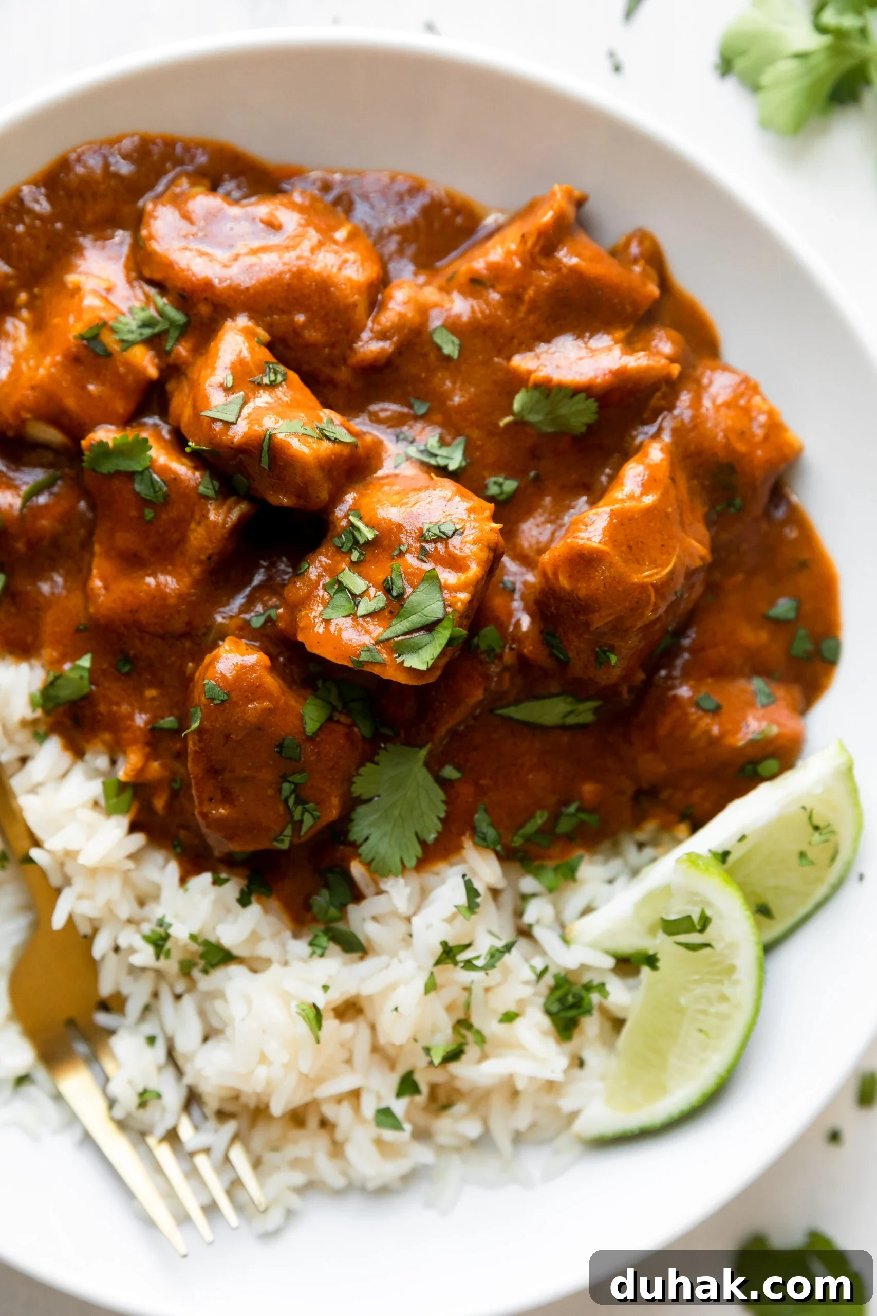 Chicken Tikka Masala Recipe: Light, Flavorful Weeknight Meal 6 a big white bowl filled with chicken tikka masala and garnished with parsley over a bed of white rice with a gold fork.