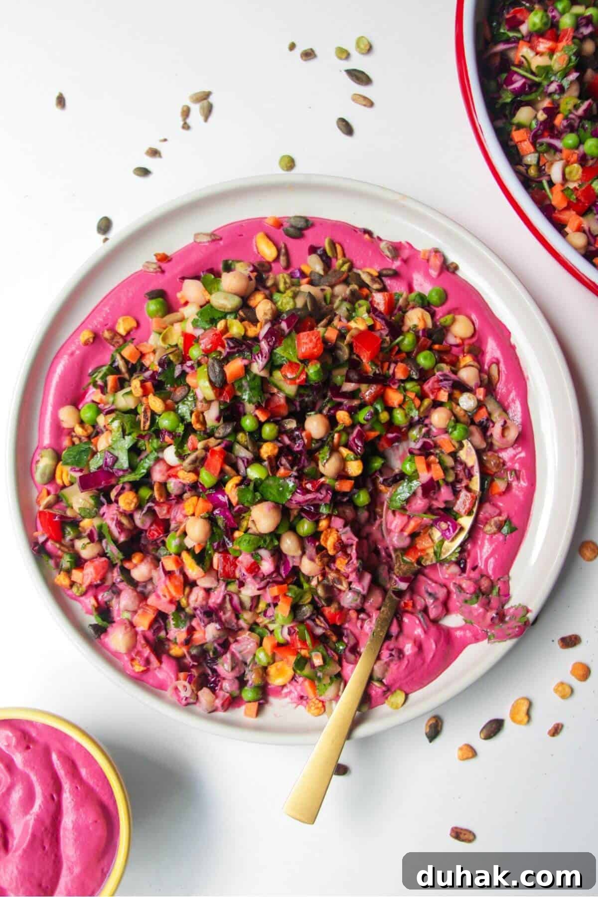 Rainbow chopped salad on pink tahini sauce on a white plate, with extra sauce on the side.