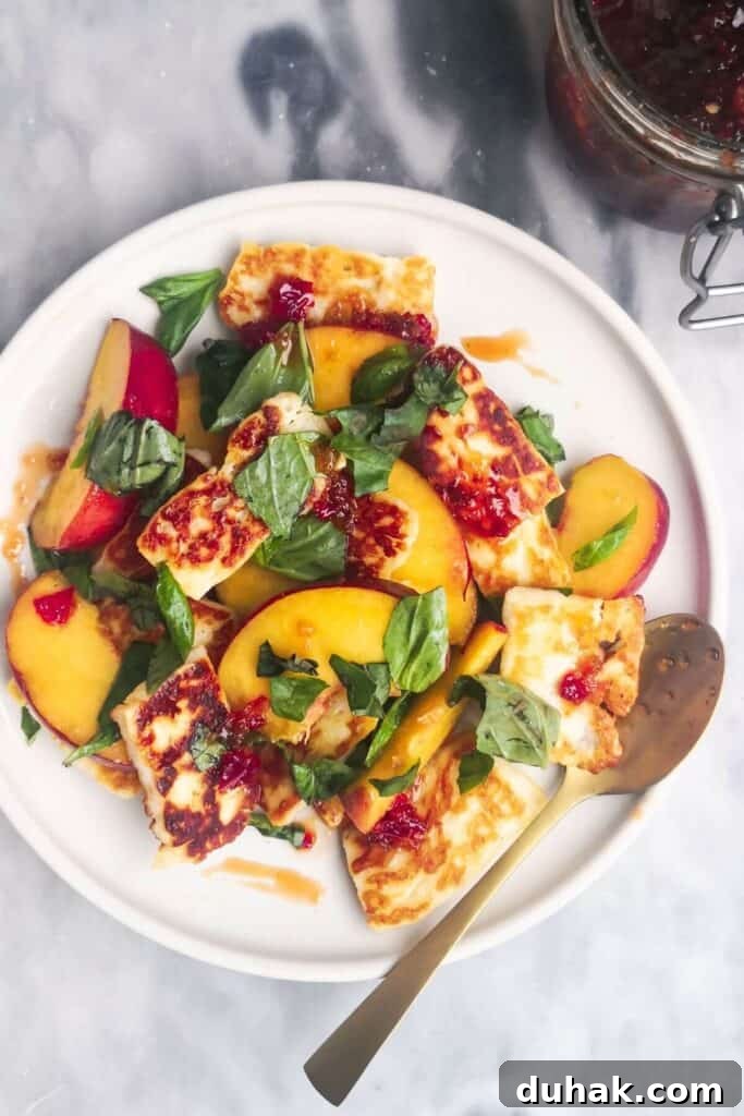 Peach and halloumi salad on a white serving plate with a small gold spoon with a jar of chilli jam in the background.