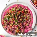Rainbow chopped salad on pink tahini sauce on a white plate, with extra sauce on the side.