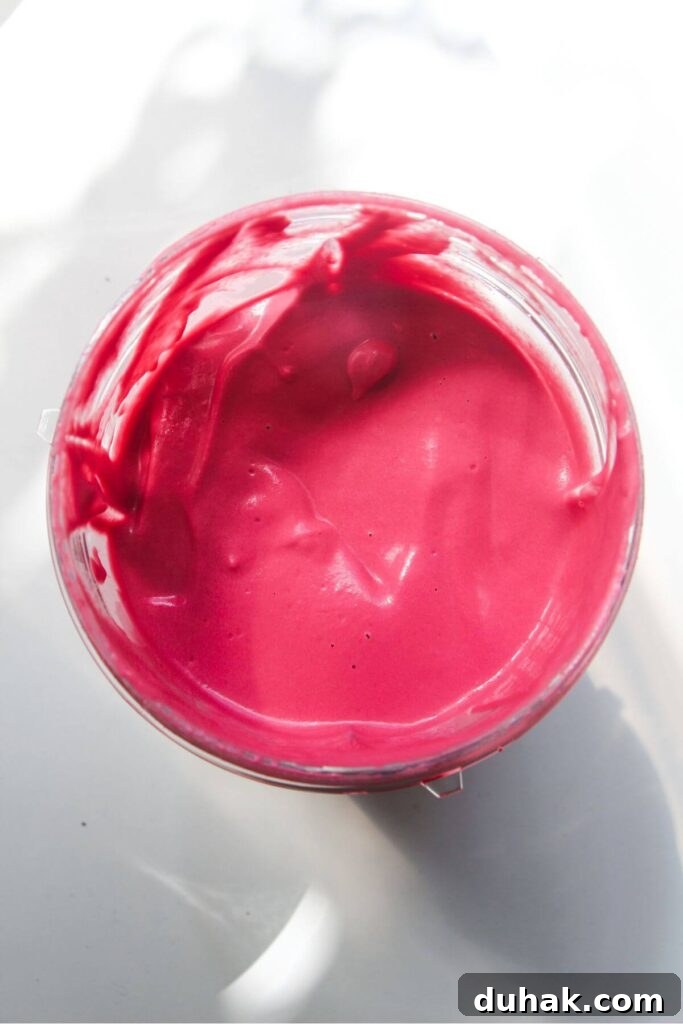 Bright pink beet tahini sauce in a clear cup.