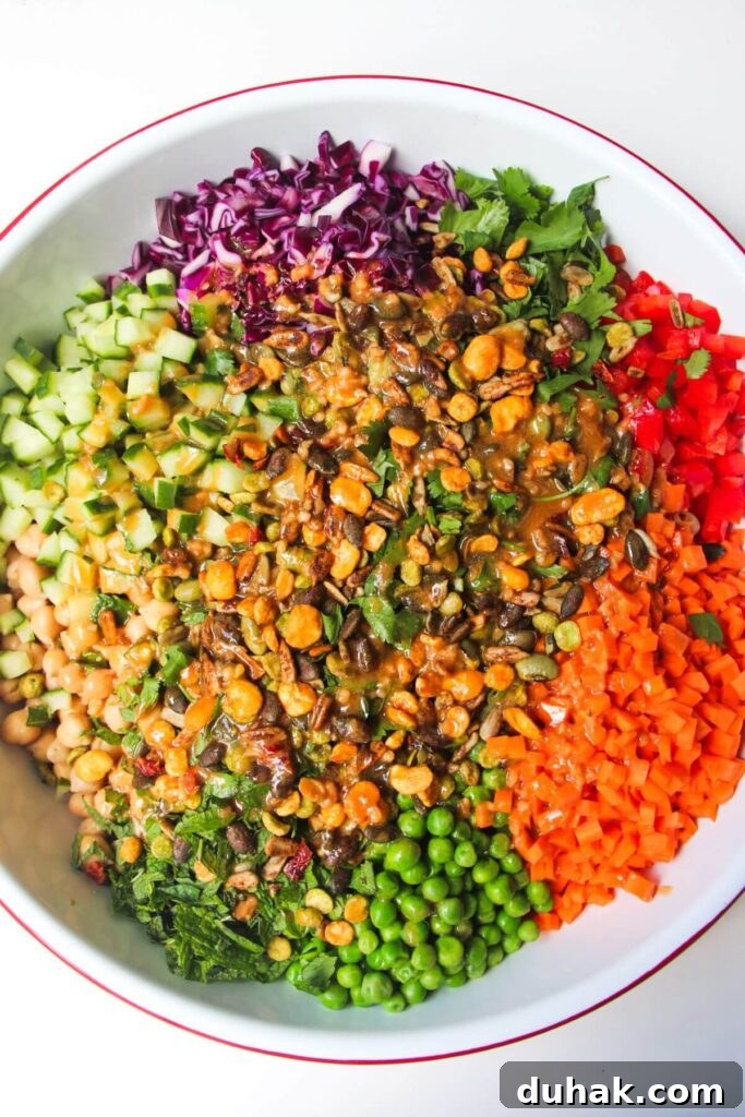 Colourful chopped vegetables in a large white bowl with dressing poured on top.