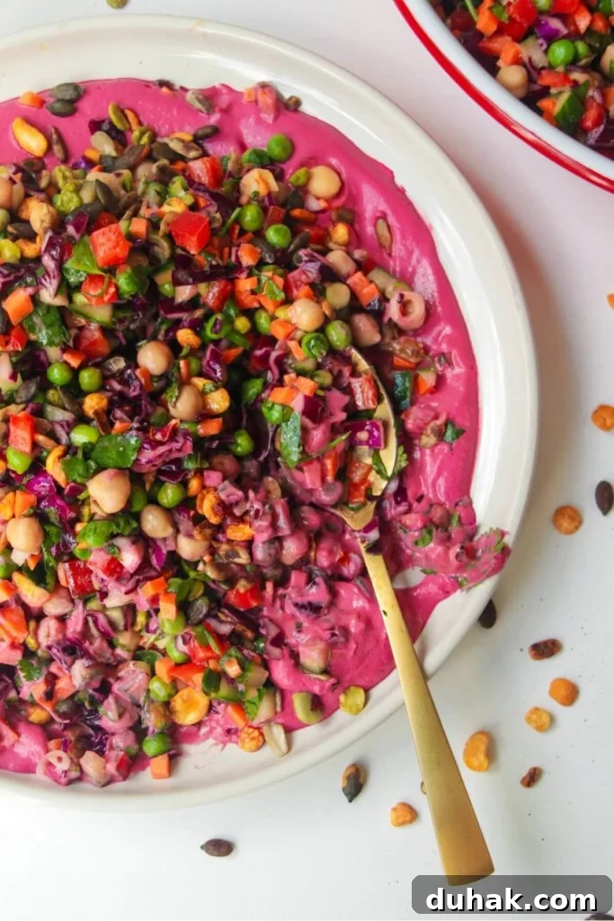 Rainbow chopped salad on pink tahini sauce on a white plate, with extra sauce on the side.