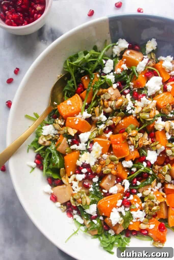 Large white and blue serving bowl with colourful butternut squash salad inside and pomegranate seeds on the side.