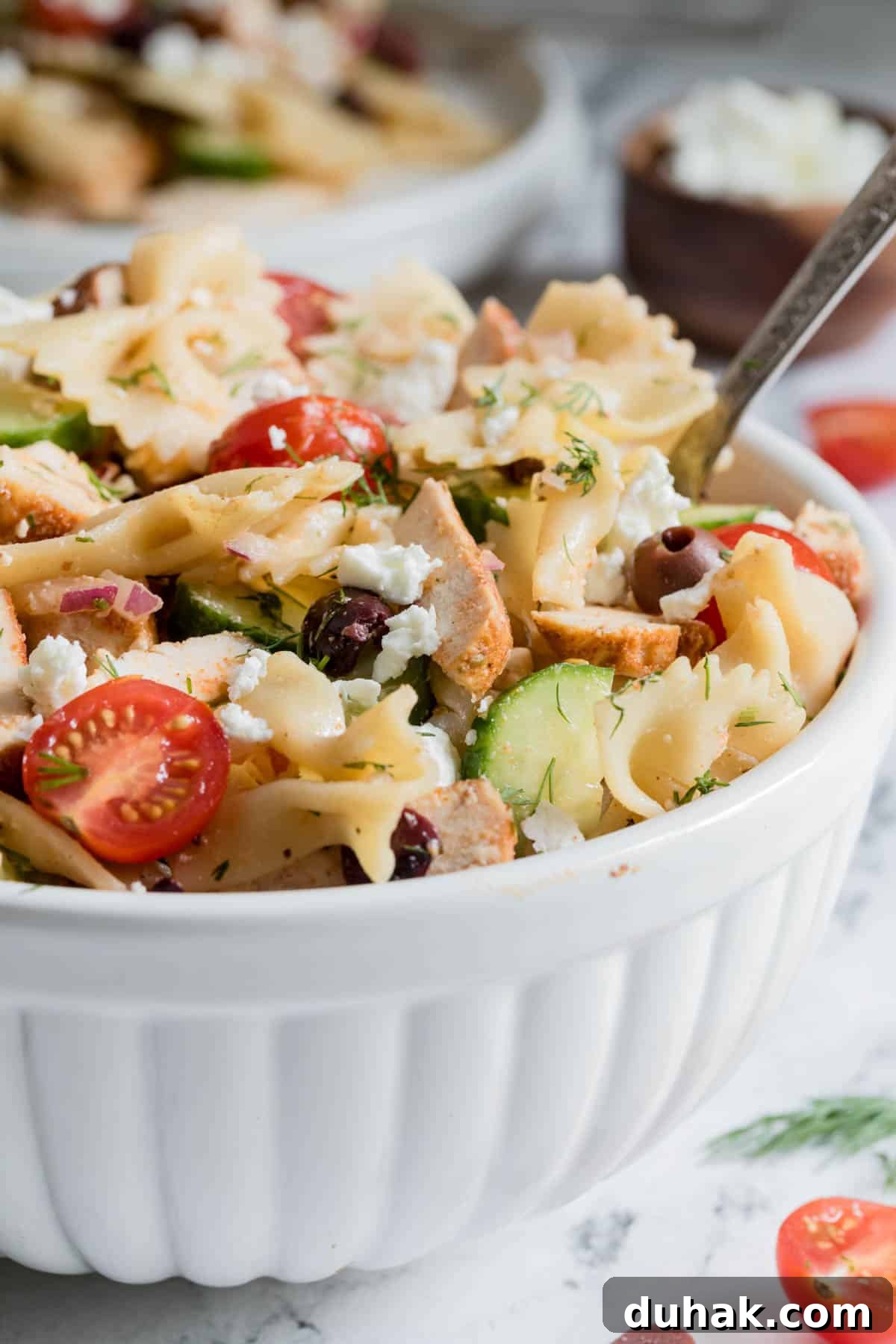 Greek Chicken Pasta Salad with Feta & Lemon Vinaigrette 4 A large serving spoon scoops the greek chicken pasta salad from the bowl.