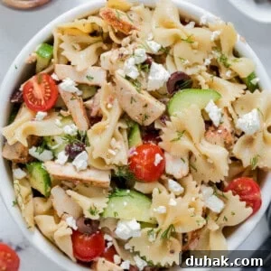 Greek Chicken Pasta Salad with Feta & Lemon Vinaigrette 5 Greek chicken pasta salad in a white bowl for serving. Cucumbers, tomatoes, kalamata olives, cooked chicken, bowtie pasta and feta cheese are piled high in the bowl.