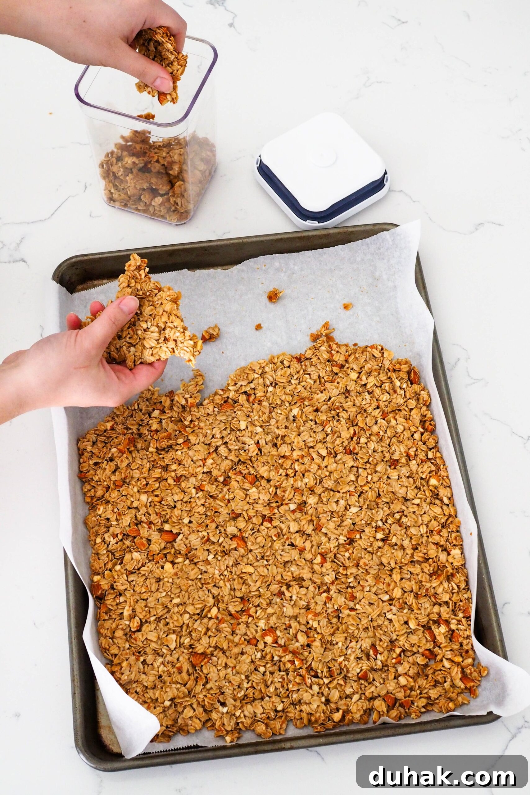 A hand breaks off a large triangle of granola from a pan.