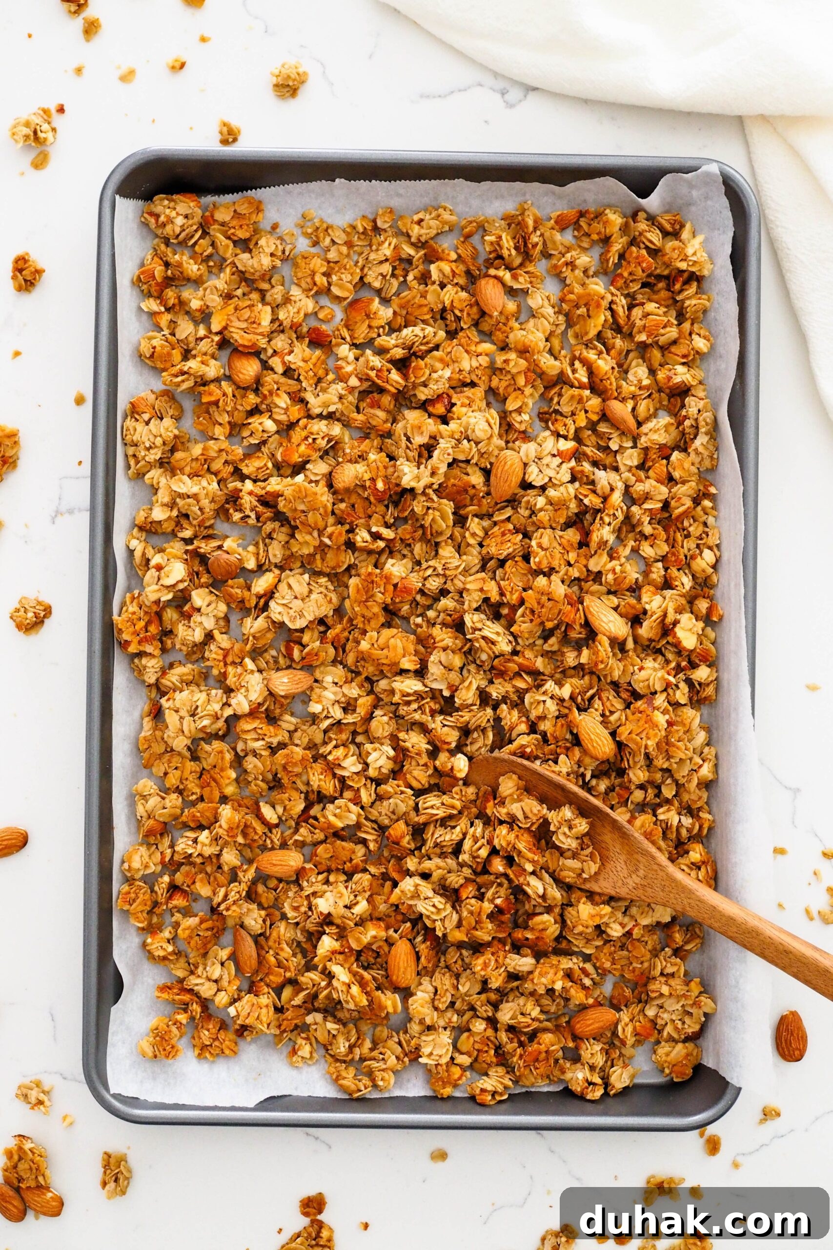 Vanilla almond granola in a baking sheet with a wooden spoon.