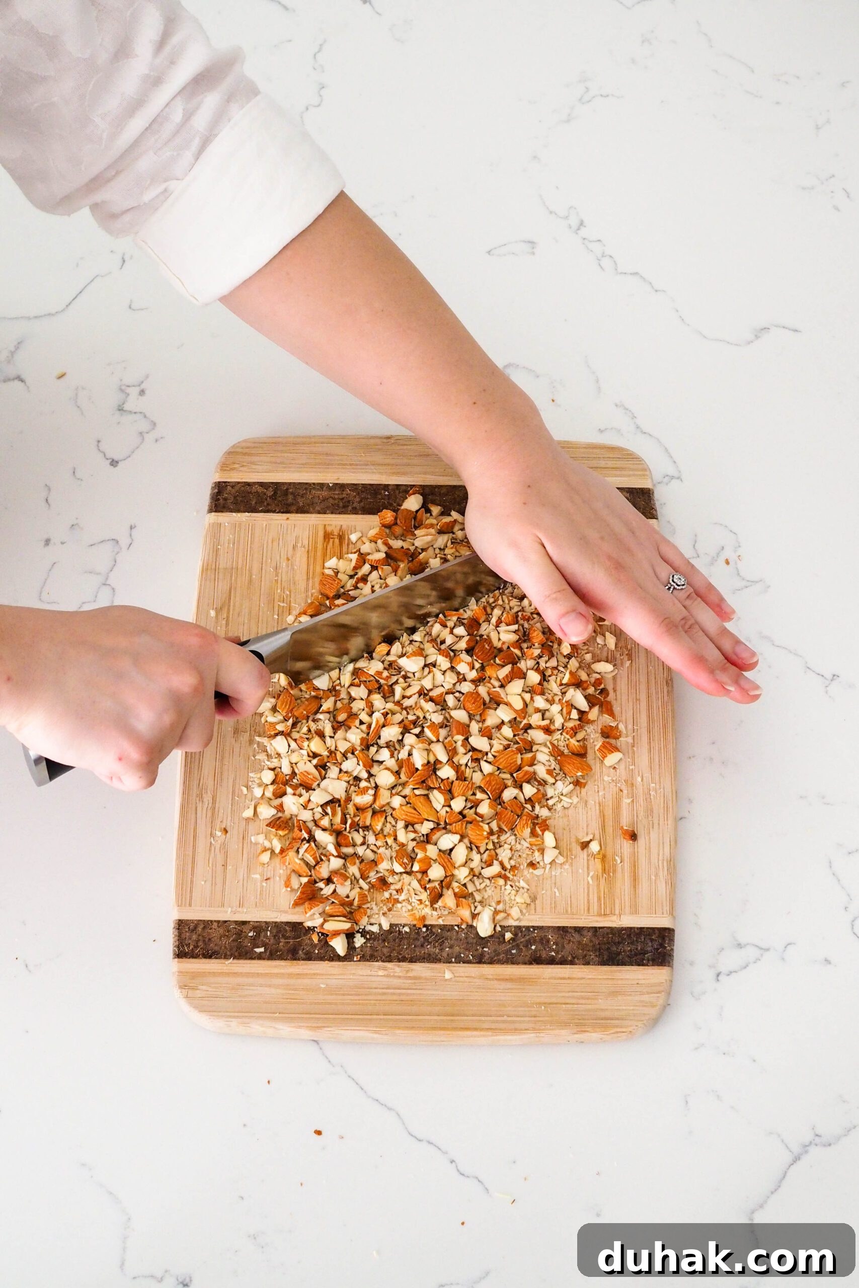 Two hands chop almonds with a chef's knife.