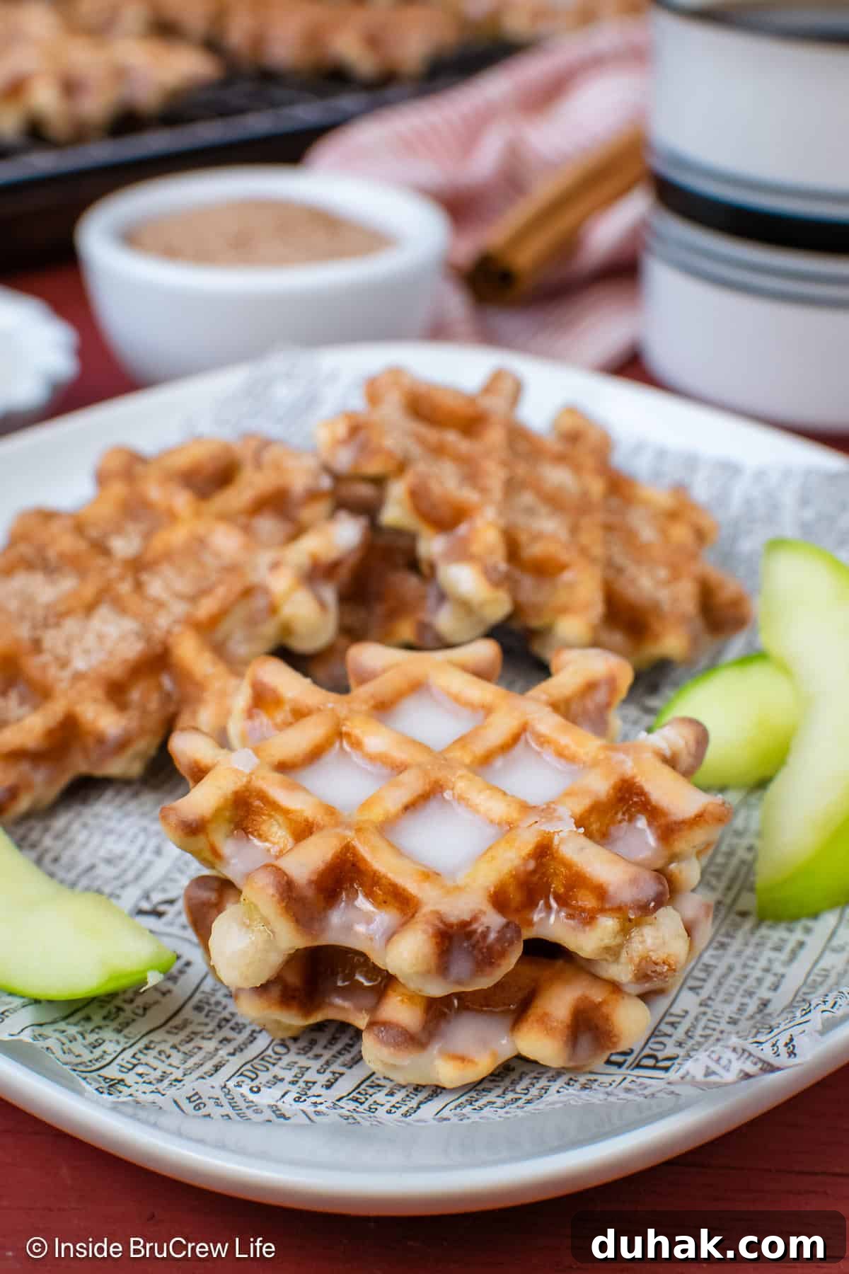 Apple waffle donuts with glaze stacked on a plate.