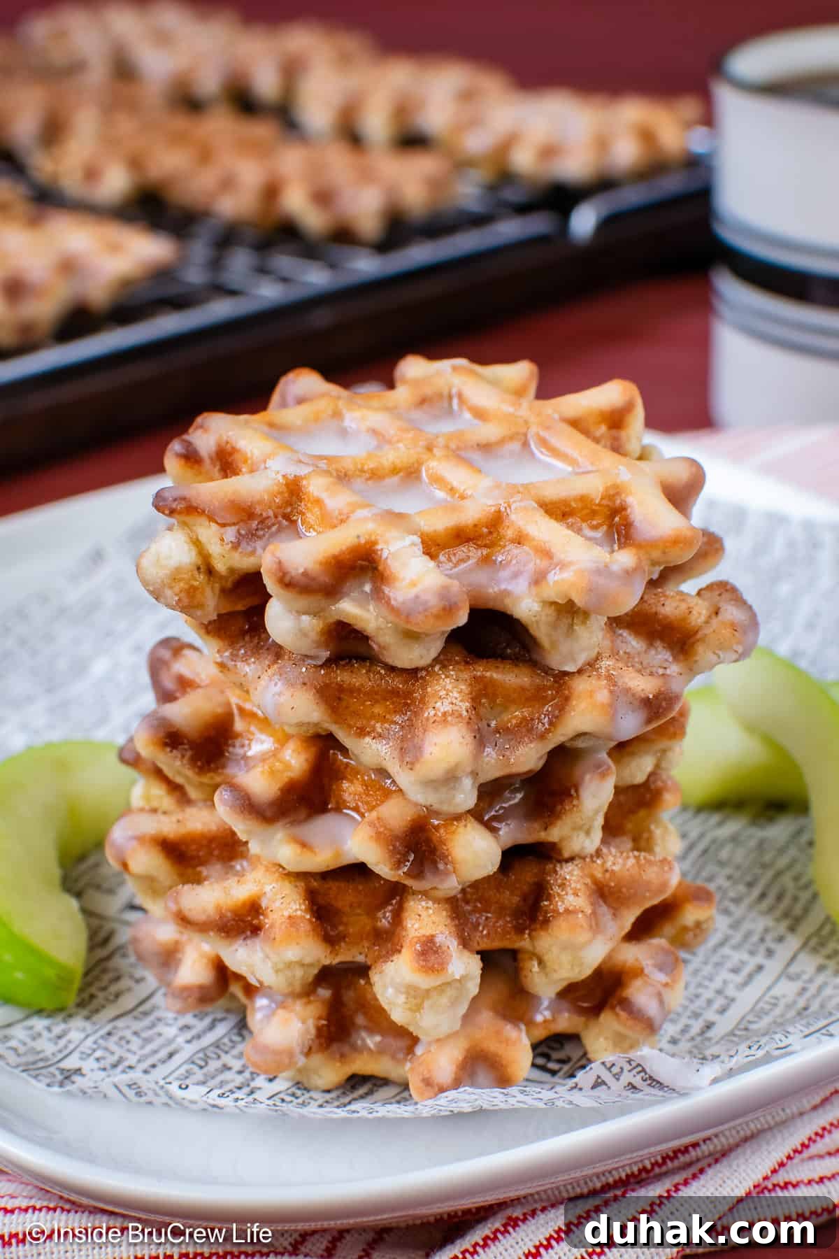 A stack of apple waffle donuts on a plate with apple slices.