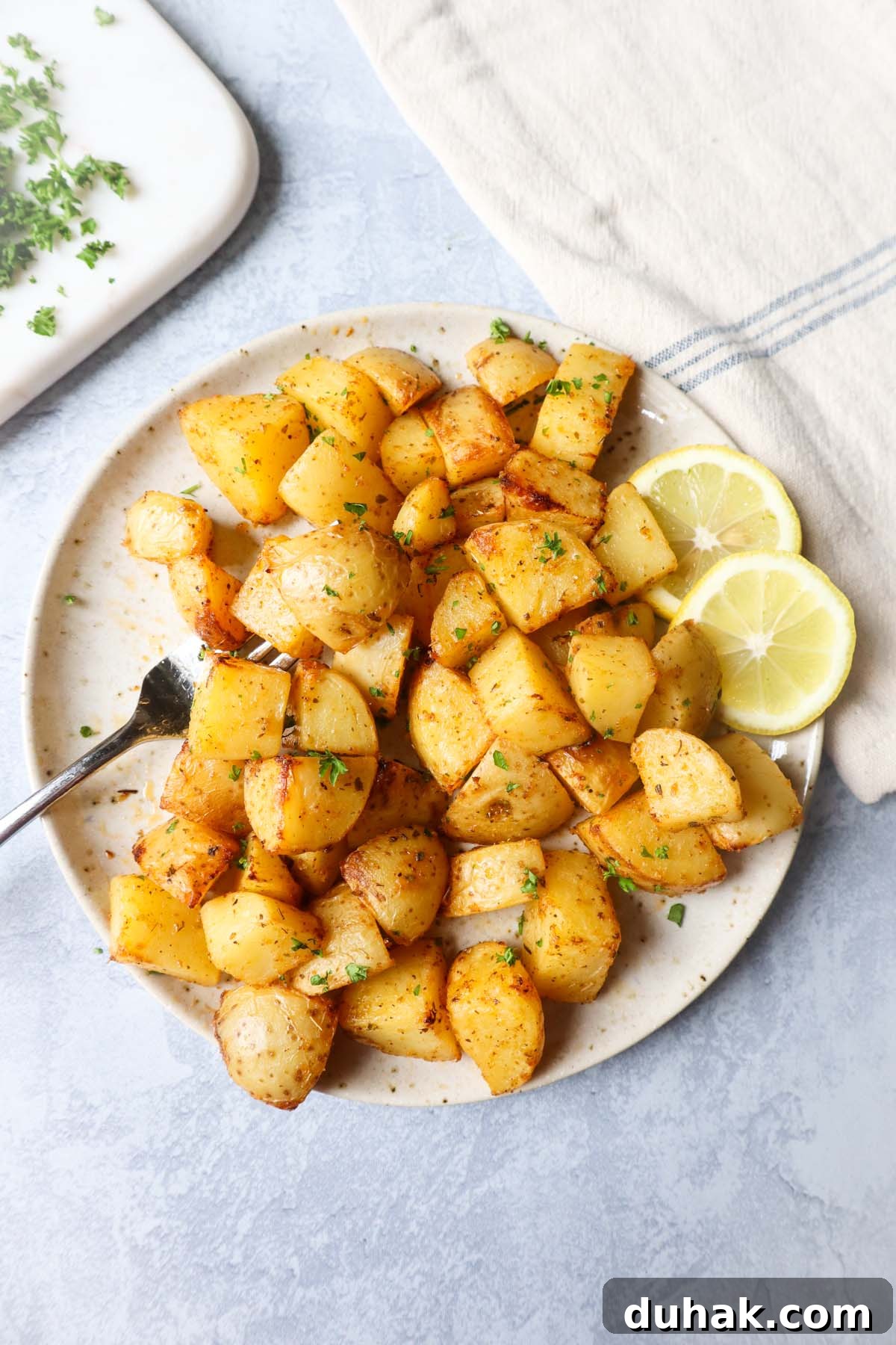 Crispy Greek-Style Potatoes in the Air Fryer 2 air fryer lemon greek potatoes on a white plate with two slices of lemon and a fork