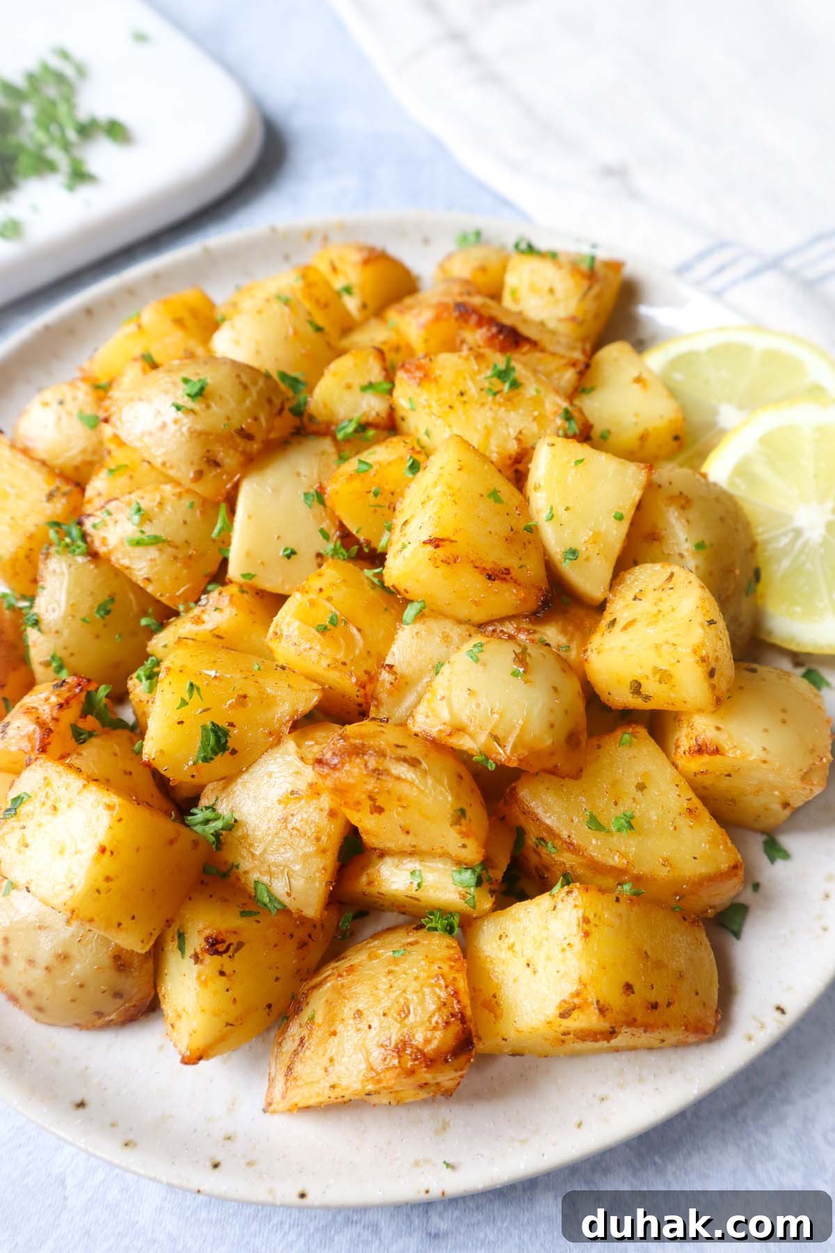 Crispy Greek-Style Potatoes in the Air Fryer 3 air fryer lemon greek potatoes on a white plate with two slices of lemon