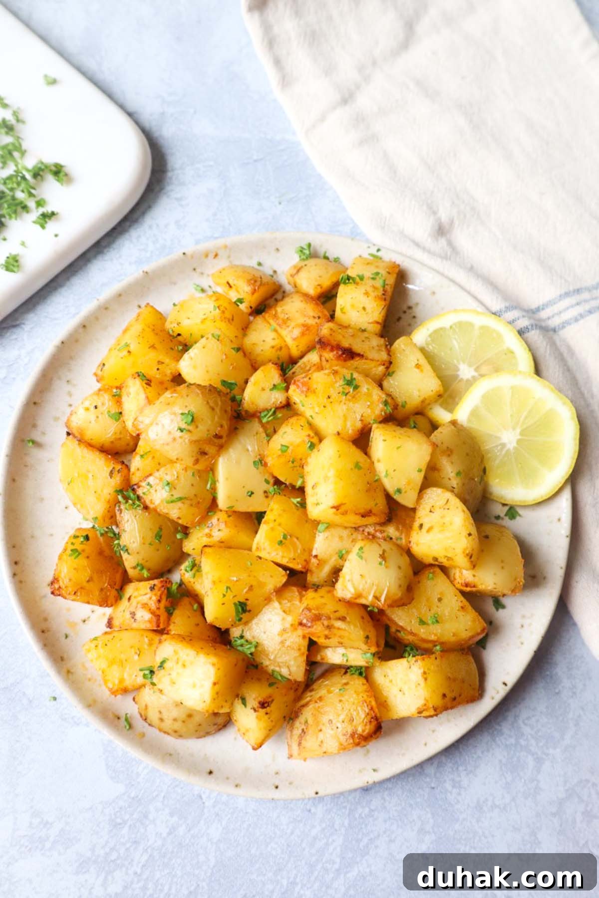 Crispy Greek-Style Potatoes in the Air Fryer 4 air fryer lemon greek potatoes on a white plate with two slices of lemon