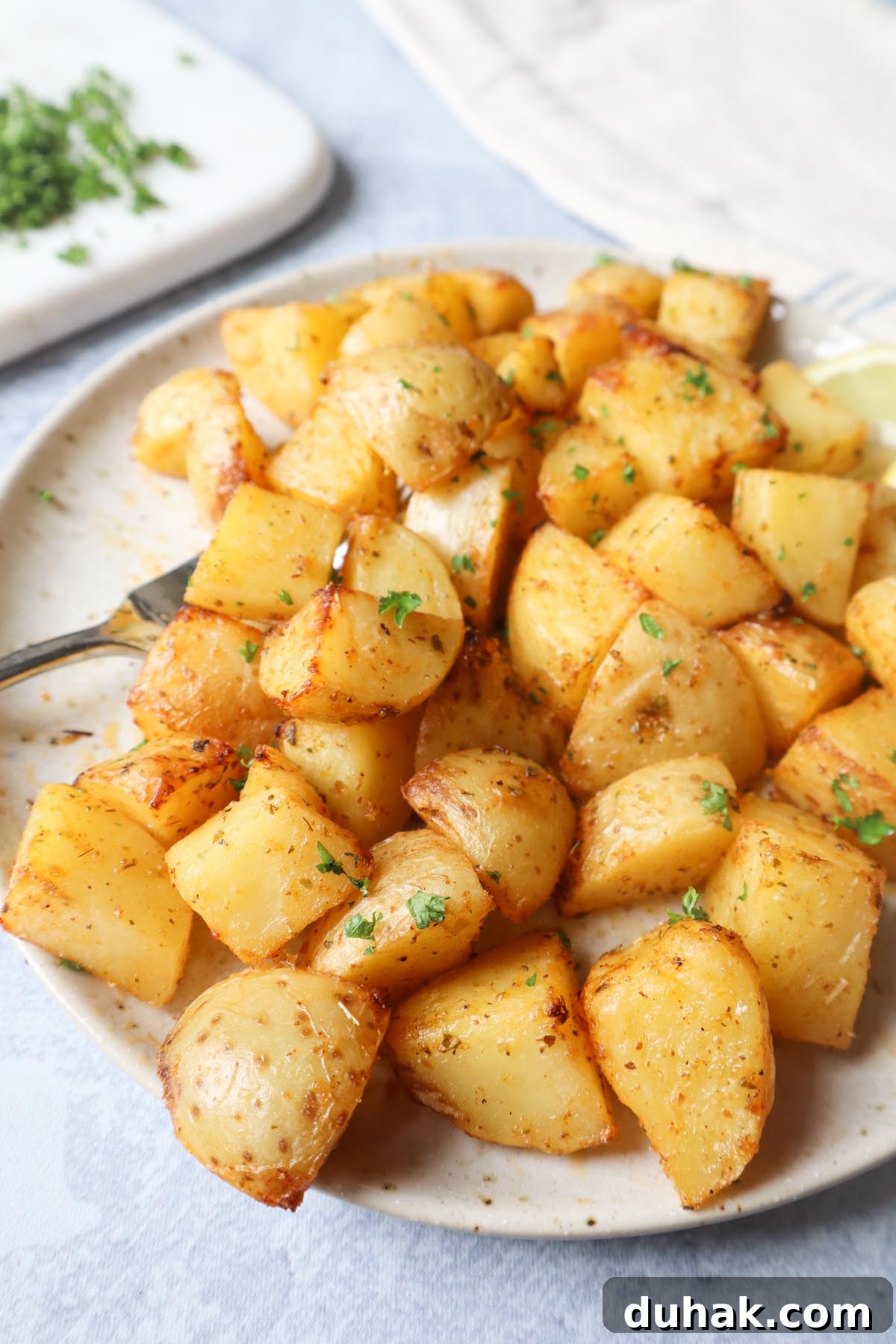 Crispy Greek-Style Potatoes in the Air Fryer 7 air fryer lemon greek potatoes on a white plate with two slices of lemon