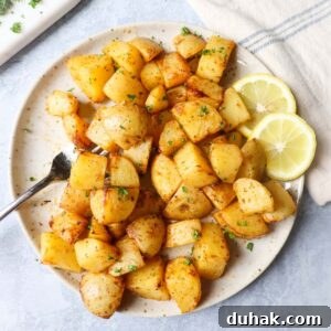 Crispy Greek-Style Potatoes in the Air Fryer 8 air fryer lemon greek potatoes on a white plate with two slices of lemon