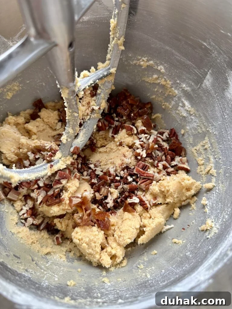 Pecan and date shortbread cookie dough in the bowl of a mixer with paddle attachment.