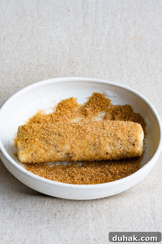 Log of shortbread cookie dough in a bowl of coarse sugar.