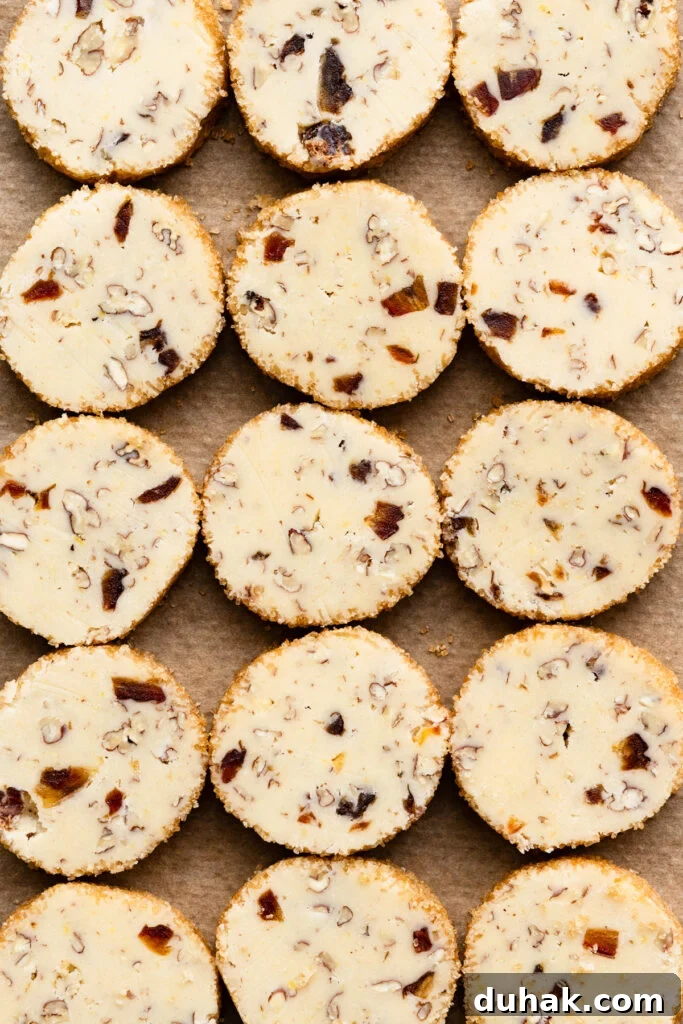 Sliced unbaked shortbread cookie dough filled with chopped pecans and dates on a tray.
