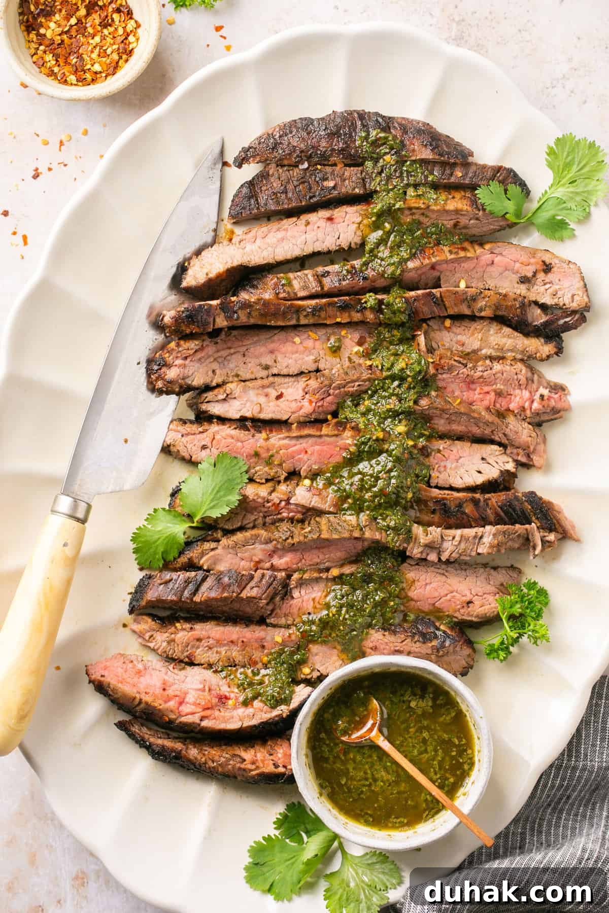 Cooked bavette steak on a white plate with chimichurri sauce on top of it with a knife beside it.