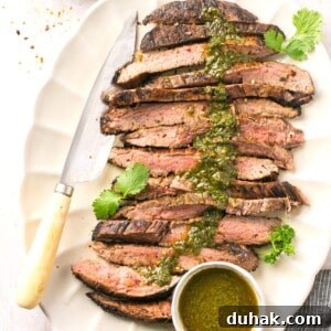 A cut bavette steak on a platter with chimichurri sauce on top.