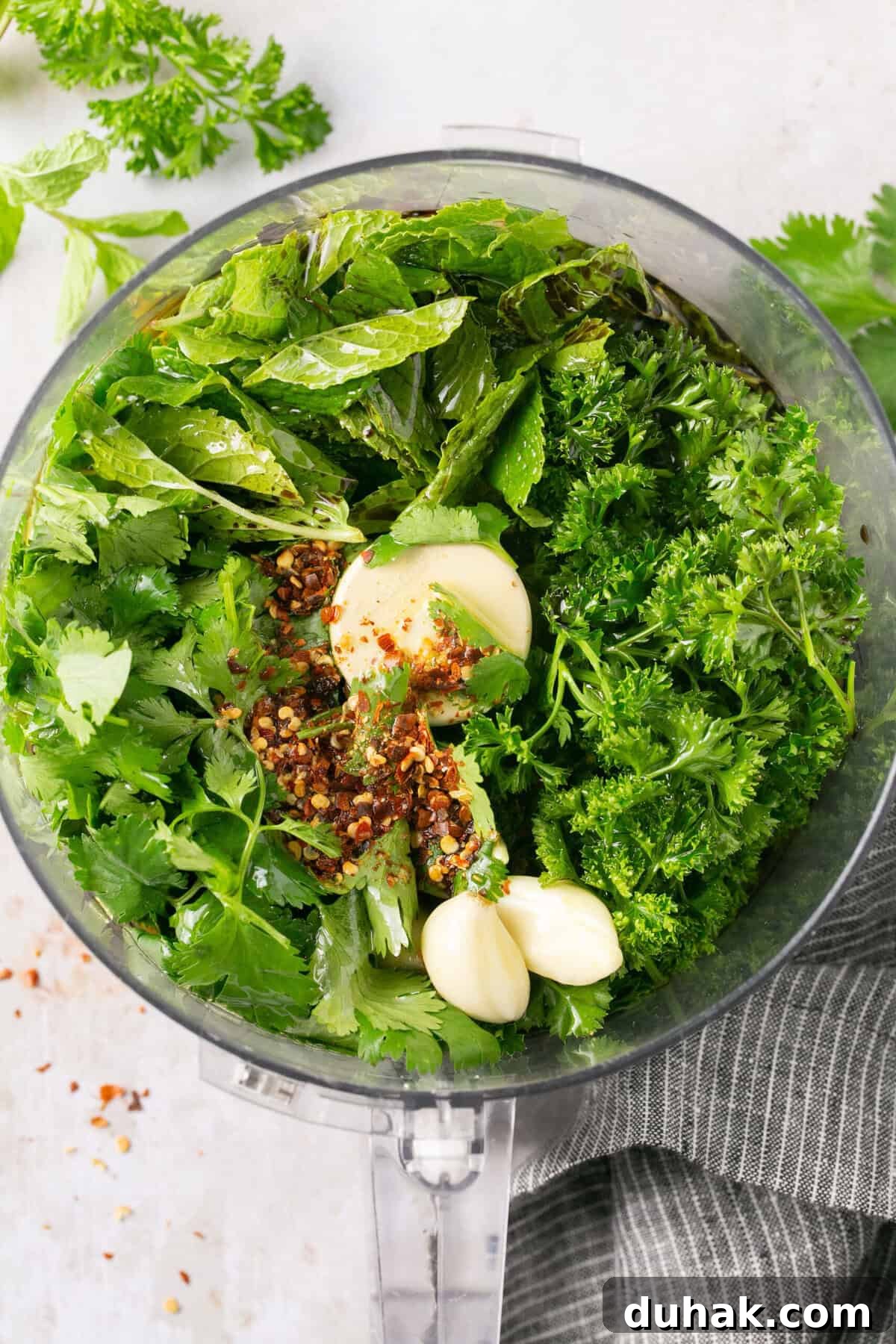 A food processor with nay different fresh herbs in it.