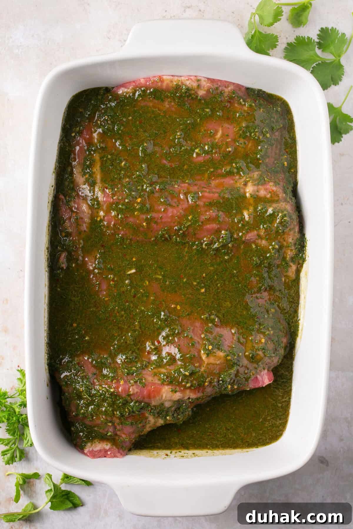 A piece of steak in a baking dish topped with chimichurri sauce.