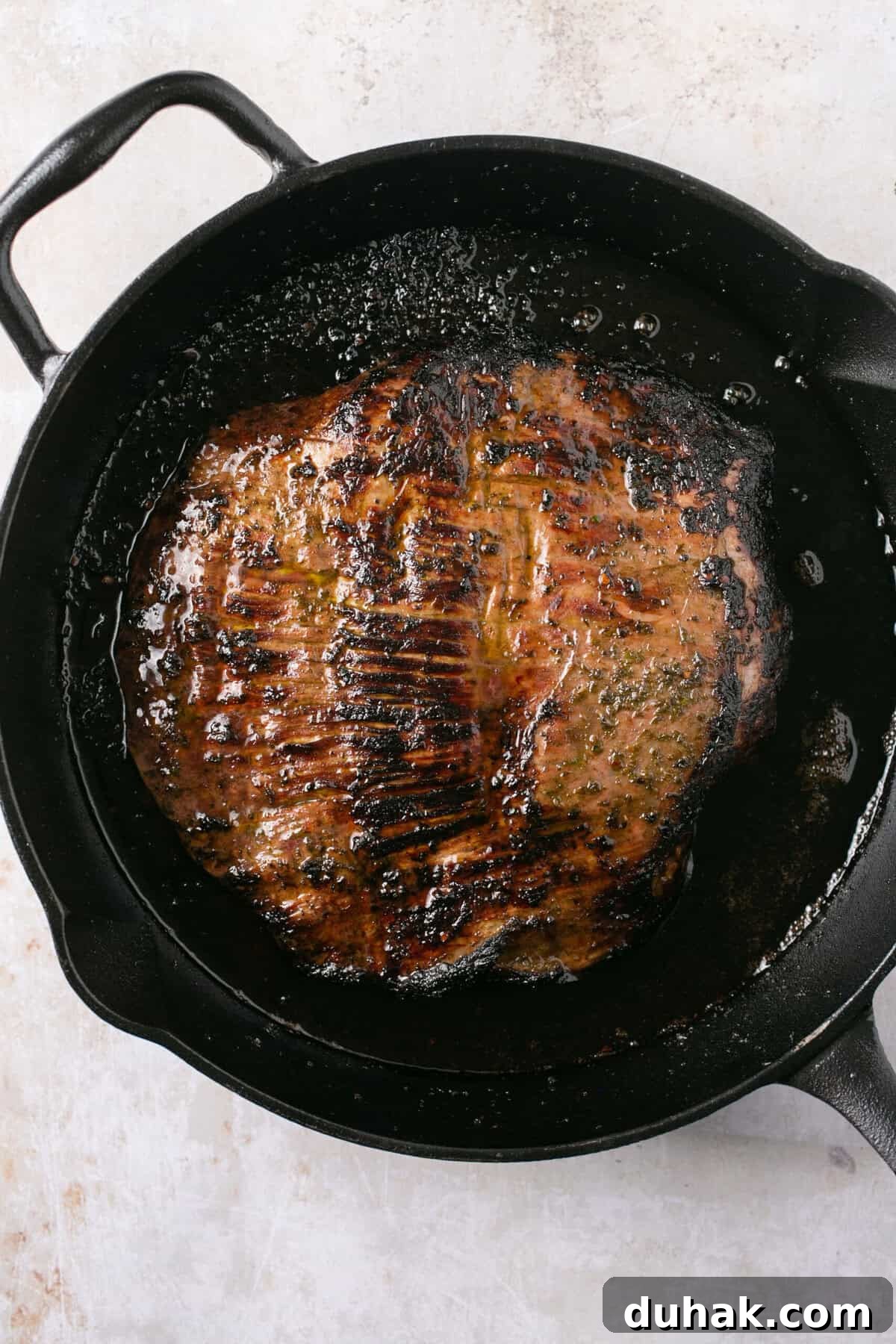 A piece of steak cooking in a cast iron skillet.