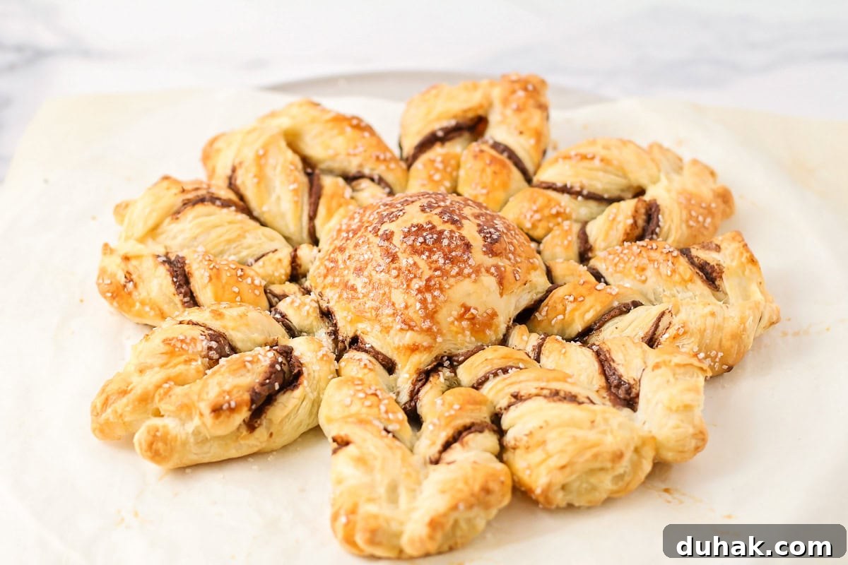 A golden brown puff pastry snowflake on a lined baking sheet.