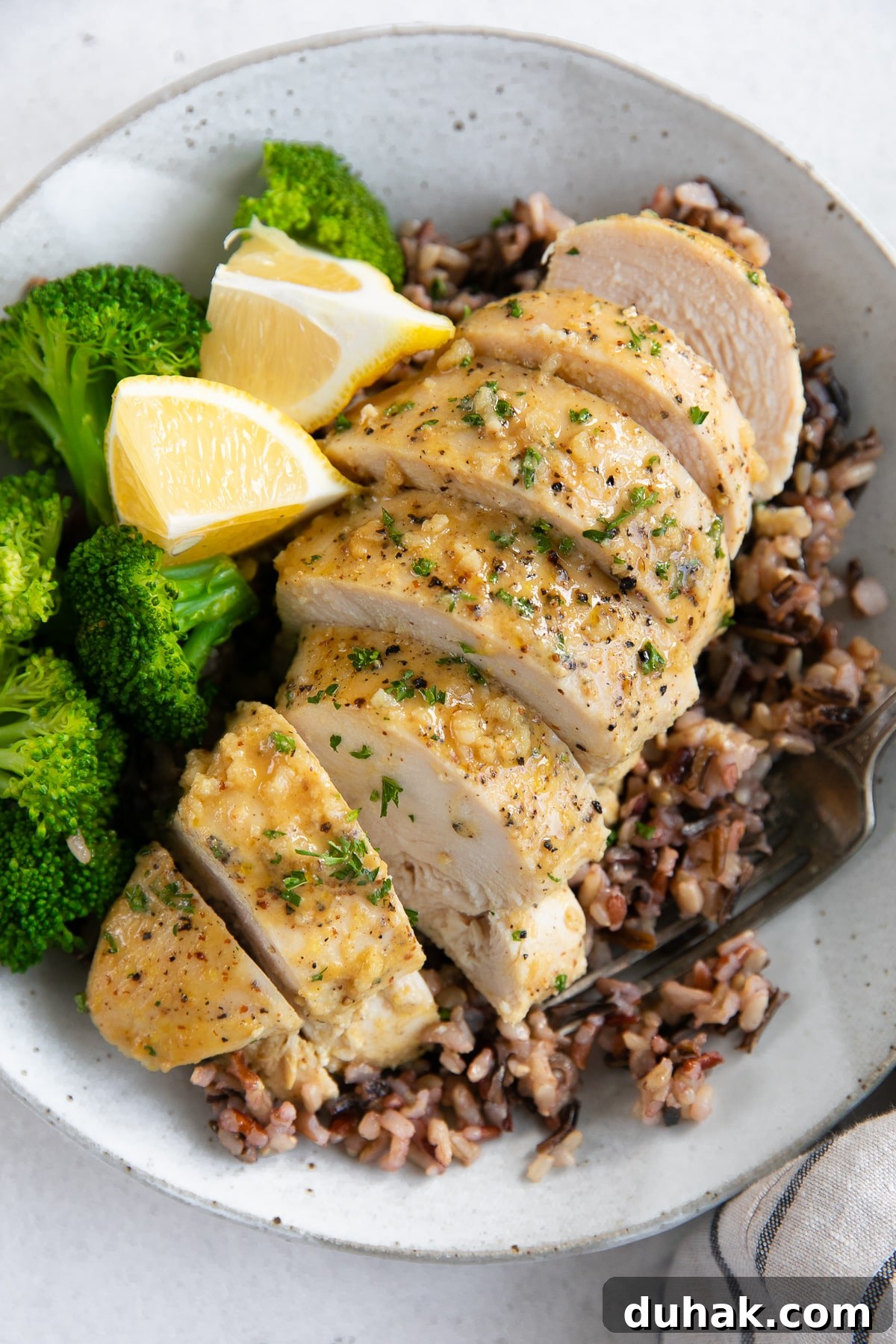 Sliced chicken breast over a bed of cooked rice and served with steamed broccoli and fresh lemon.