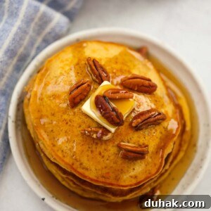 a stack of sweet potato pancakes with pecans, butter, and maple syrup.