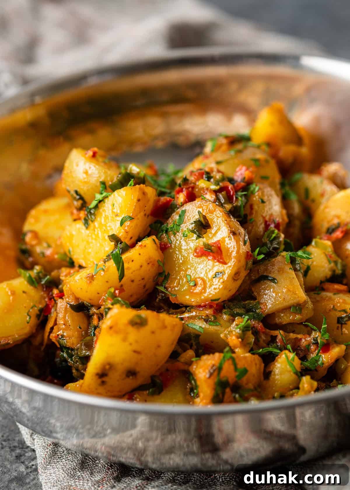Spicy Calabrian Potatoes with Garlic and Chili Peppers 9 closeup: calabrian chili potatoes topped with fresh chopped herbs in a metal bowl
