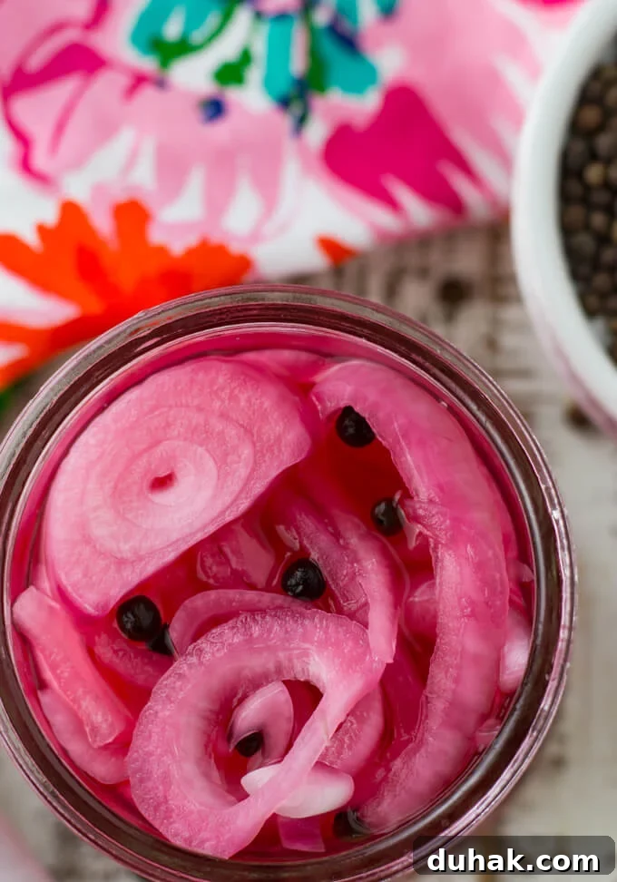 An overhead photo of pickled red onions. A colorful pink napkin and a bowl fo allspice berries sit next to the onions. 