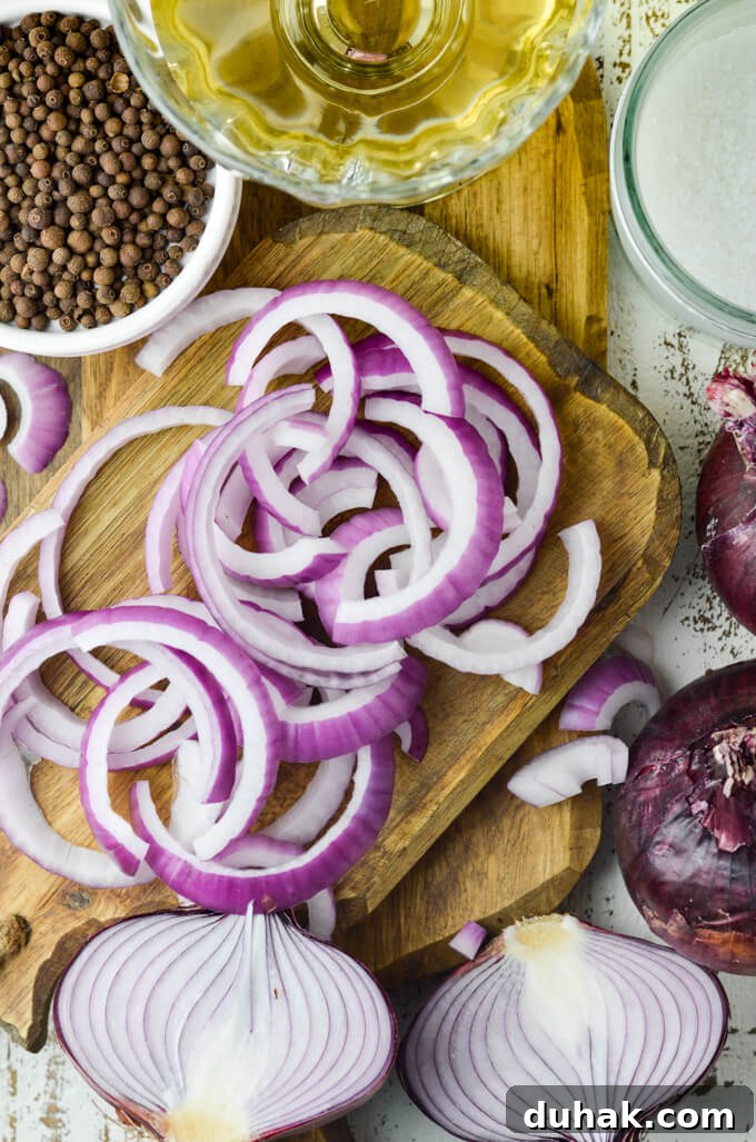  A cutting board holds slices of red onions. Allspice berries are in a bowl beside them. A clear bowl of vinegar and a jar of sugar are in the corner of the photo.