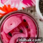 An overhead photo of pickled red onions. A colorful pink napkin and a bowl fo allspice berries sit next to the onions.