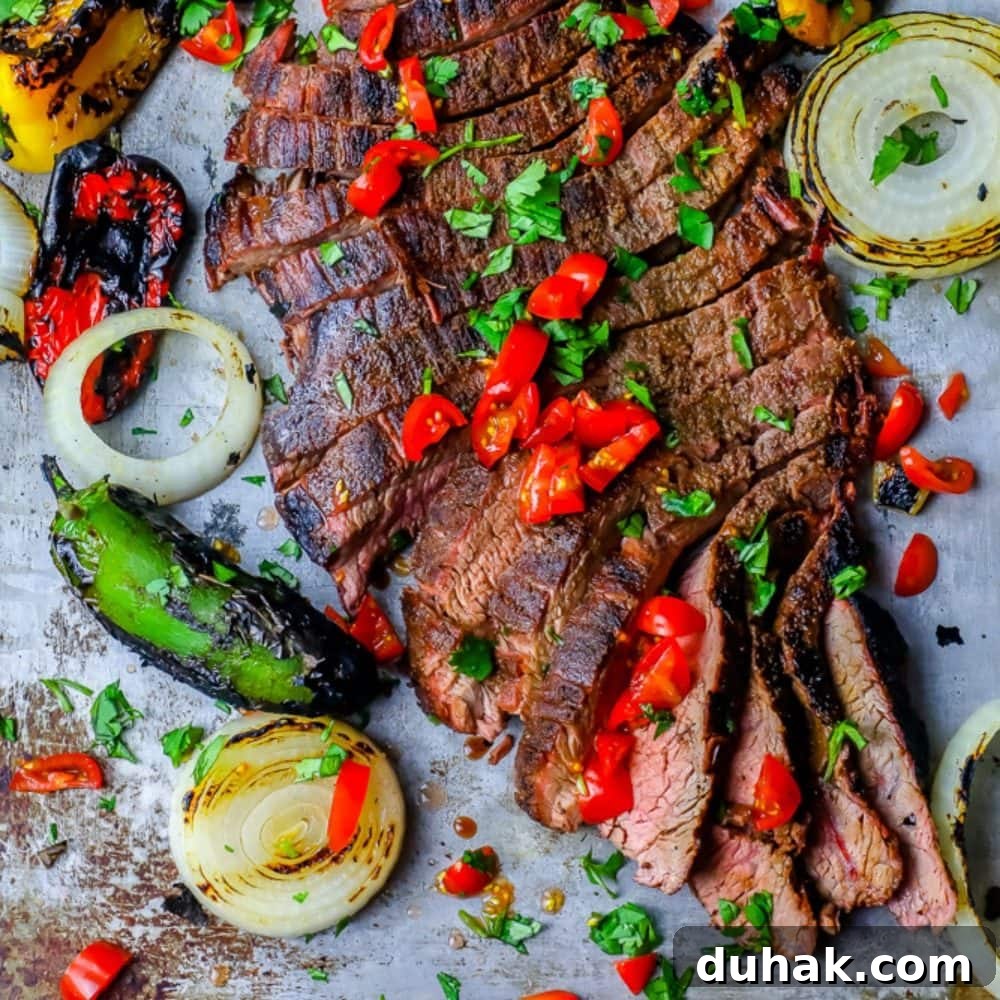 The Best Grilled Carne Asada Recipe Ever featuring a steak cooked with peppers and onions on a baking sheet.
