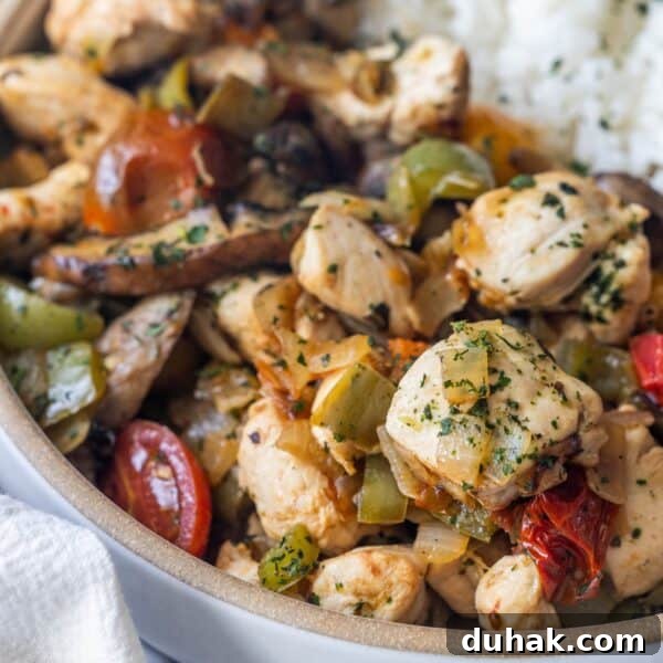 A close-up of a bowl filled with cooked chicken pieces, bell peppers, tomatoes, and herbs—this Keto Italian Chicken Skillet Dinner is served with a portion of white rice visible in the background.