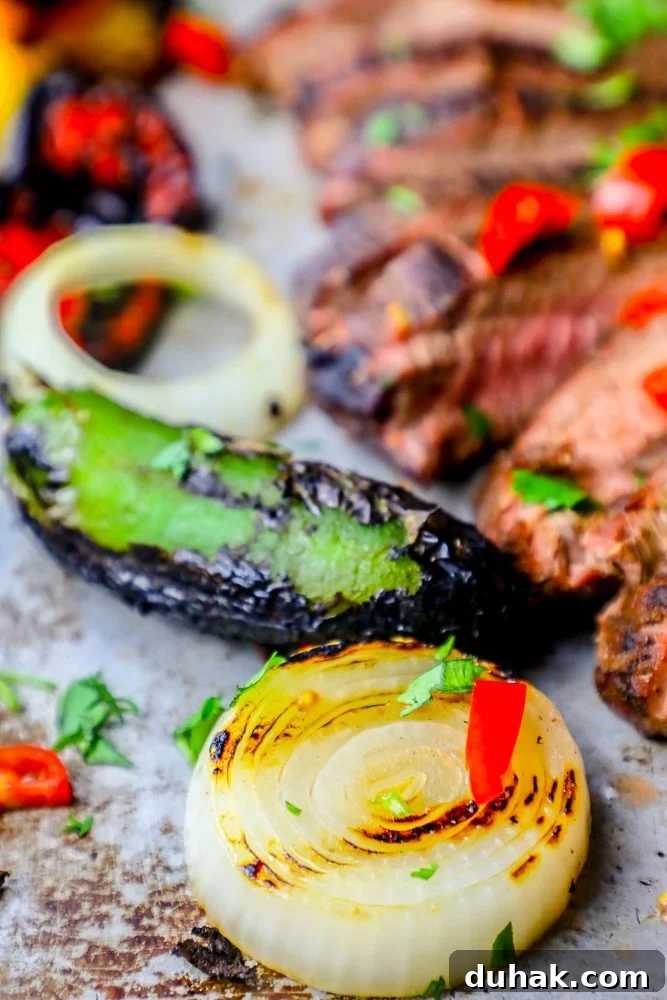 Grilled carne asada fajitas recipe with onions and peppers on a baking sheet.
