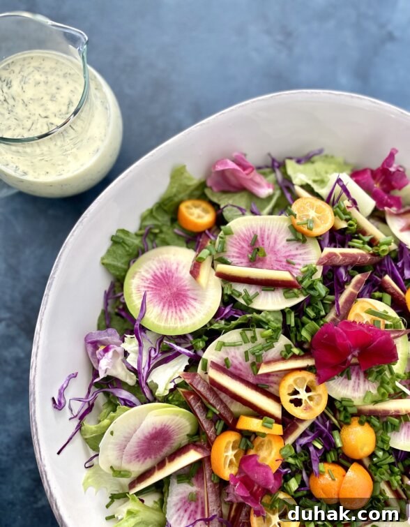 a spring salad in a white platter next to a container of dill dressing
