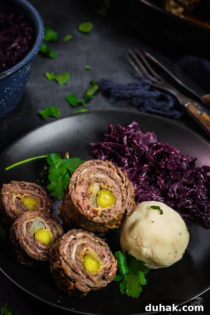 A shot of a sliced German beef roll ups served on a black plate with red cabbage and dumpling, on a dark background