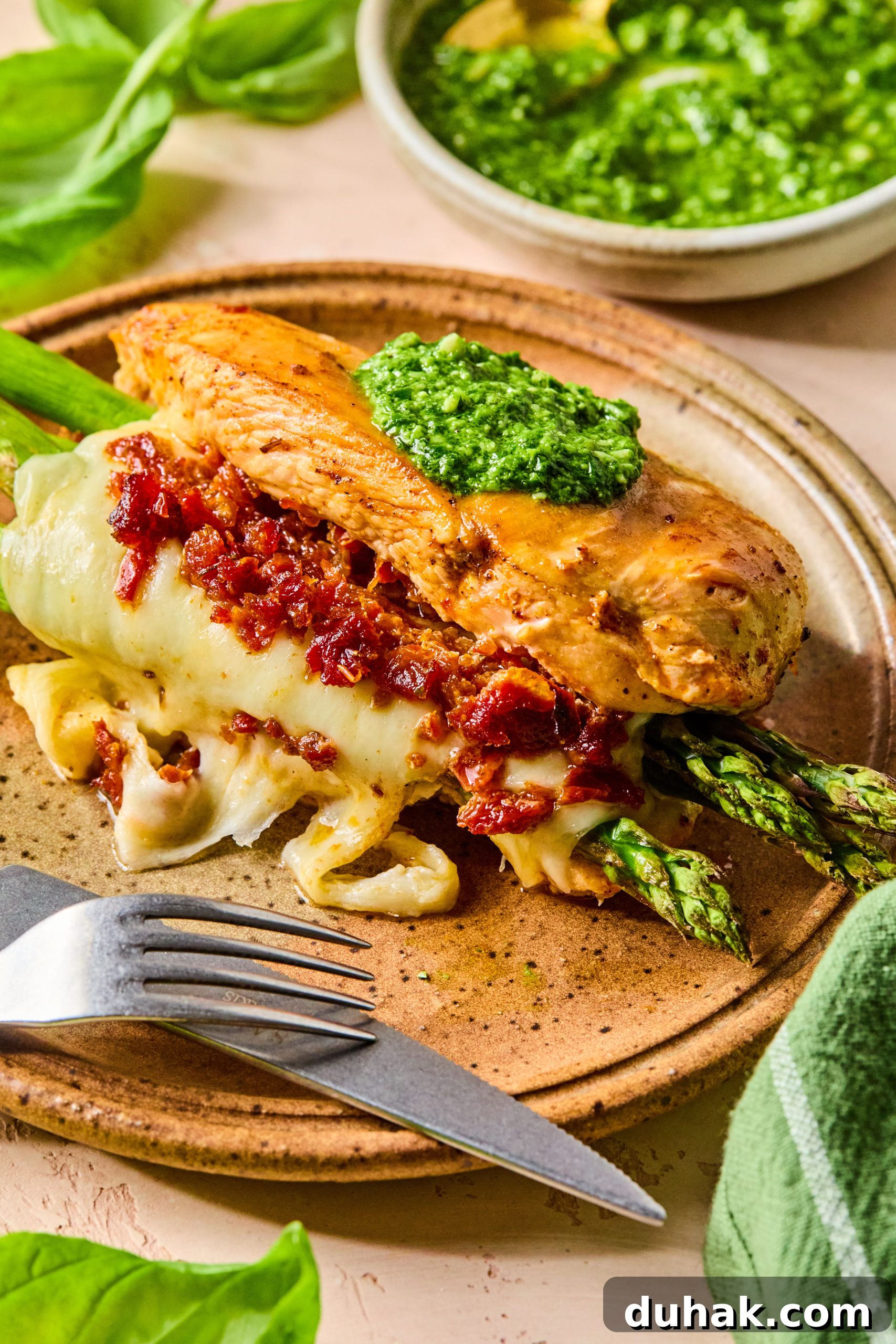 Asparagus and Sun-Dried Tomato Stuffed Chicken with Pesto and Cheese 11 A close up photo of asparagus stuffed chicken made with melty mozzarella cheese, sun-dried tomatoes and a dollop of homemade pesto on top
