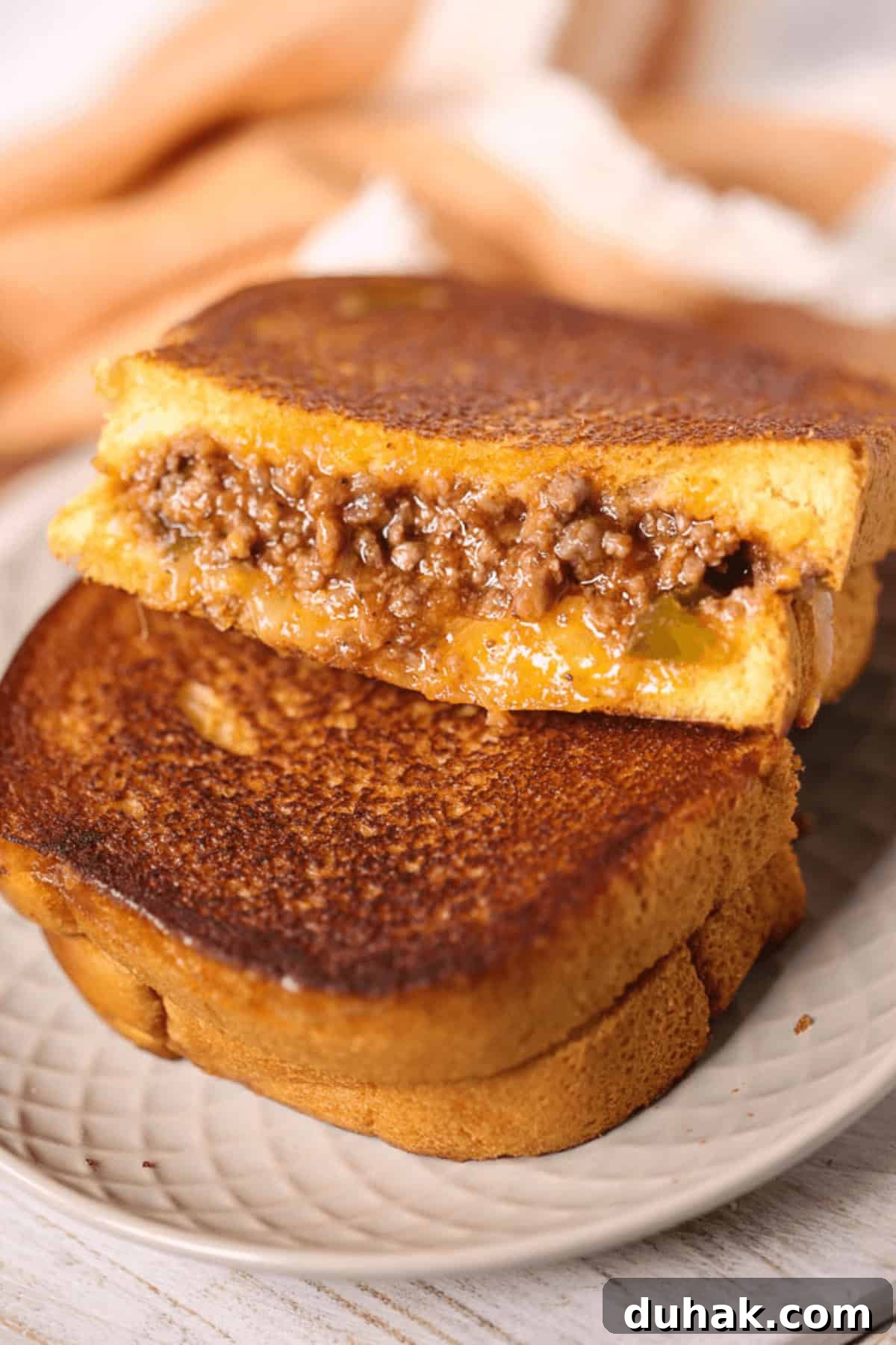 Sloppy Joe Grilled Cheese Sandwich Recipe for Comfort Dinner 2 A Sloppy Joe Grilled Cheese sandwich, brimming with melted cheese and savory ground beef filling, is expertly grilled, cut in half, and elegantly stacked on a plate.