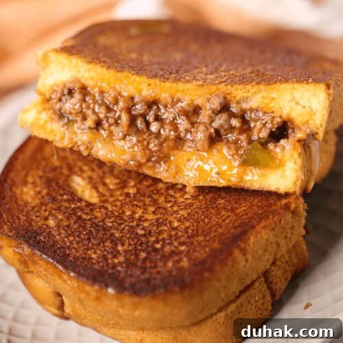 Sloppy Joe Grilled Cheese Sandwich Recipe for Comfort Dinner 7 A Sloppy Joe Grilled Cheese sandwich, brimming with melted cheese and savory ground beef filling, is expertly grilled, cut in half, and elegantly stacked on a plate.
