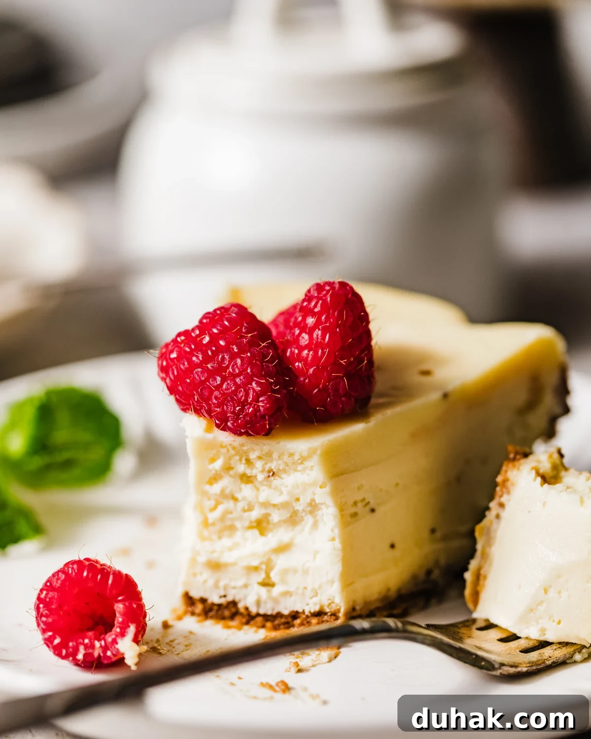 Silky Mascarpone Cheesecake Recipe with Luscious Cream Filling 2 a slice of mascarpone cheesecake on a plate with fresh raspberries and mint.