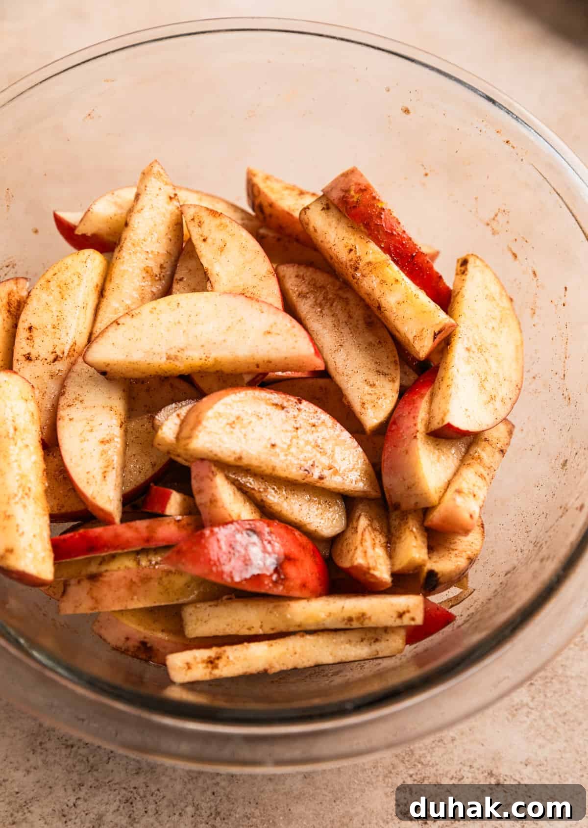 Apples sliced and tossed in oil and cinnamon in glass mixing bowl